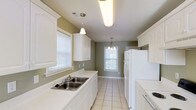 This single-floor, 2-bedroom, 2-bathroom home offers a comfortable and well-organized layout designed for easy everyday living. The kitchen is a standout feature, styled in a classic galley configuration with crisp white cabinetry that extends to the upper and lower walls, providing ample storage space. The countertops are clean and light-toned, complementing the white double-basin sink and white appliances, including a full-size refrigerator and range. Light tile flooring runs throughout the kitchen, adding a bright and airy feel to the space. Two windows allow generous natural light to filter in, creating a welcoming atmosphere. Pendant lighting — including a small chandelier near the dining area — adds a touch of elegance to the functional space. The soft sage-green wall color ties the kitchen together with a warm, neutral palette. The overall ambiance of the home is clean, bright, and inviting, with thoughtful details that balance practicality and charm. The single-floor layout ensures seamless flow between spaces, making this home an ideal, low-maintenance residence suitable for a variety of lifestyles.