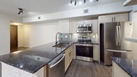 This 960-square-foot, single-story apartment at 7921 Venture Center Way in Boynton Beach, Florida offers a well-designed 2-bedroom, 1-bathroom layout across a thoughtfully organized floor plan. The open-concept kitchen and living area serves as the heart of the unit, featuring dark hardwood-style flooring, track lighting, and a peninsula with dark granite countertops and an undermount sink. The kitchen is equipped with stainless steel appliances including a refrigerator, range, microwave, and dishwasher, complemented by gray shaker-style cabinetry and a green subway tile backsplash. The spacious living room flows naturally from the kitchen and includes a ceiling fan and sliding glass doors that open to an outdoor view, allowing natural light to fill the space. Both bedrooms are carpeted and feature ceiling fans; each includes its own closet. The primary bedroom measures 150 square feet and offers access to additional closet space. A total of three closets are distributed throughout the unit. The bathroom includes a tiled tub-shower combination with classic white subway tile, a granite-topped vanity, and tile flooring. A dedicated laundry area houses a stacked Whirlpool washer and dryer, adding everyday convenience to this functional Boynton Beach residence.