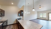 This well-appointed single-floor home offers a thoughtfully designed open-concept layout that seamlessly connects the kitchen, dining, and living areas. The kitchen is a standout feature, showcasing rich dark-stained cabinetry with sleek bar-pull hardware, light granite countertops, a deep undermount sink, and a breakfast bar peninsula. Stylish pendant lighting hangs above the peninsula, complementing the open sightlines into the living space. Vaulted ceilings elevate the main living area, enhancing its sense of openness and airiness, while durable wood-look plank flooring runs throughout the main areas.

The bathroom is finished with matching dark cabinetry, marble-look countertops, a soaking tub, and wood-look flooring, maintaining a cohesive design aesthetic. The bedroom features plush carpeting, a ceiling fan, and a window that welcomes natural light. Adjacent to the bedroom, a generously sized walk-in closet is outfitted with multi-level wire shelving systems, providing ample organized storage. A second walk-in closet offers additional storage capacity.

The dedicated laundry room includes a full-size GE washer and dryer alongside overhead wire shelving and a granite folding surface. Completing the home is a spacious attached single-car garage with an automatic opener, offering convenient direct access.