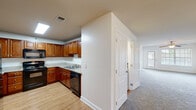 Located at 5111 Parcstone Ln in Fayetteville, NC, this single-story home offers a thoughtfully organized layout with a neutral, move-in-ready aesthetic throughout. The kitchen is a functional highlight, featuring rich medium-toned wood cabinetry with raised panel doors, granite countertops, hardwood-style flooring, and black appliances including a refrigerator and dishwasher. Ample upper and lower cabinet storage, including a tall pantry-style cabinet, ensures generous organization space.

The living areas are carpeted and finished with clean white walls and ceiling fans with integrated lighting, contributing to a bright and comfortable atmosphere. Natural light filters in through windows, enhancing the open feel of the main living space, which also includes a fireplace surround visible in one area.

The bedrooms are carpeted with neutral tones and white trim, providing versatile spaces. A spacious walk-in closet features wire shelving and hanging rods on multiple walls for ample storage. The bathrooms include tub and shower combinations with chrome fixtures. Hardwood-style flooring carries through the bathroom areas, tying the overall design together cohesively.