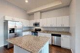 Located at 18248 W 12 Mile Rd in Southfield, Michigan, this well-appointed 2-bedroom, 2-bathroom residence offers a thoughtfully designed single-floor layout with a generous sense of space throughout. The open-concept living, dining, and kitchen area serves as the heart of the home, anchored by a modern kitchen featuring white shaker cabinetry, granite countertops, a central island, and a full suite of stainless steel appliances including a side-by-side refrigerator, range, microwave, and dishwasher. Dark hardwood-style flooring flows through the main living areas, adding warmth and contrast to the neutral palette. The living room is highlighted by floor-to-ceiling sliding glass doors that flood the space with natural light and open onto a private balcony with outdoor views. Both bedrooms are generously sized with plush carpet flooring, elevated ceilings with architectural beam details, and ample closet space. The primary bedroom is notably spacious, offering a comfortable retreat. The bathrooms are finished with large-format tile and a sleek glass-enclosed shower. Additional conveniences include a dedicated laundry area, a welcoming entrance corridor, and three closets for abundant storage throughout.