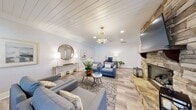 Located at 2350 Houston Lake Rd in Perry, Georgia, this thoughtfully designed single-room space offers a refined blend of comfort and functionality. The room is anchored by a dramatic floor-to-ceiling stacked-stone fireplace, which serves as the undeniable focal point and lends a warm, rustic-elegant character to the otherwise crisp, modern interior. A wall-mounted television above the fireplace mantel adds a practical entertainment element.

The ceiling features white shiplap paneling accented by crown molding, recessed lighting, and a decorative geometric pendant light with brass hardware, contributing to an airy and polished ambiance. Light wood-look luxury vinyl plank flooring runs throughout, enhancing the brightness of the neutral, white-walled interior.

The space is organized into distinct functional zones: a comfortable lounge area with blue upholstered seating and a patterned area rug, and a dedicated workspace equipped with a wooden desk and ergonomic chair. Natural light filters in through windows, complemented by strategically placed floor and table lamps. A decorative console table with a round mirror and gold-accented furnishings adds an elegant finishing touch. This space is ideal for use as a living room, office, or multi-purpose retreat.