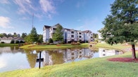 Located at 1001 Bear Island Rd in Summerville, South Carolina, this residential community offers a welcoming environment defined by well-maintained grounds and attractive architectural design. The multi-story buildings feature a classic blue and neutral exterior palette accented by dark rooflines, private balconies, and large windows that invite natural light throughout. The community is set against a backdrop of mature trees and carefully manicured landscaping, contributing to a serene, park-like atmosphere. A prominent scenic pond anchors the exterior grounds, its calm surface reflecting the buildings and surrounding greenery, creating a picturesque setting that enhances the overall ambiance of the property. The lush, open lawn areas surrounding the pond provide generous outdoor space, adding to the sense of openness and tranquility. The community's layout emphasizes connectivity between buildings and natural outdoor spaces, making it an inviting environment for residents. Positioned in Summerville, SC, the property benefits from the area's characteristic Southern charm, temperate climate, and access to local amenities, making it a compelling residential destination in the Lowcountry region.