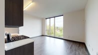 Located at 4011 NE Cleveland Ave in Portland's vibrant NE neighborhood, this thoughtfully designed single-floor unit offers a clean, contemporary aesthetic throughout. Wide-plank wood-style flooring flows seamlessly from the entry hallway into the main living areas, complemented by crisp white walls and dark accent baseboards that create a modern, polished look.

The open kitchen is a standout feature, equipped with a full suite of stainless steel appliances including a gas range, over-the-range microwave, dishwasher, and refrigerator. Dark espresso cabinetry extends to the ceiling, providing generous storage, while light countertops and a tile backsplash add a clean, contemporary contrast.

The living area is bathed in natural light through expansive floor-to-ceiling windows that frame lush treetop views of the surrounding Portland neighborhood. Additional rooms, ideal for bedrooms or flex spaces, also benefit from large windows offering abundant daylight and neighborhood views.

A sleek entry corridor with recessed lighting leads to the unit's front door, finished with a modern charcoal panel design. The bathroom features matching dark cabinetry, a white vanity countertop, and wood-style flooring, maintaining the cohesive design language found throughout the space.