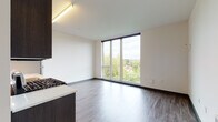 Located at 4011 NE Cleveland Ave in Portland's vibrant NE neighborhood, this thoughtfully designed single-floor unit offers a clean, contemporary aesthetic throughout. Wide-plank wood-style flooring flows seamlessly from the entry hallway into the main living areas, complemented by crisp white walls and dark accent baseboards that create a modern, polished look.

The open kitchen is a standout feature, equipped with a full suite of stainless steel appliances including a gas range, over-the-range microwave, dishwasher, and refrigerator. Dark espresso cabinetry extends to the ceiling, providing generous storage, while light countertops and a tile backsplash add a clean, contemporary contrast.

The living area is bathed in natural light through expansive floor-to-ceiling windows that frame lush treetop views of the surrounding Portland neighborhood. Additional rooms, ideal for bedrooms or flex spaces, also benefit from large windows offering abundant daylight and neighborhood views.

A sleek entry corridor with recessed lighting leads to the unit's front door, finished with a modern charcoal panel design. The bathroom features matching dark cabinetry, a white vanity countertop, and wood-style flooring, maintaining the cohesive design language found throughout the space.