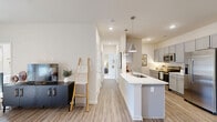 This thoughtfully designed 2-bedroom, 2-bathroom residence offers a comfortable and functional single-level layout with a clean, contemporary aesthetic. The open-concept living, dining, and kitchen area serves as the heart of the home, filled with natural light and anchored by light-toned wood-look flooring that flows throughout the main spaces. The living room features a ceiling fan, neutral walls, and glass doors that open to an outdoor area, enhancing the sense of airiness. The kitchen is well-equipped with gray shaker-style cabinetry extending to the ceiling, white quartz countertops, stainless steel appliances including a full-size refrigerator, electric range, built-in microwave, and dishwasher, along with a tile backsplash and a peninsula with pendant lighting. The adjacent dining area provides a welcoming space for meals. The primary bedroom is generously sized with large windows, plush carpet, and a ceiling fan, while the second bedroom features a bold accent wall and cozy carpet flooring. Both bathrooms are well-appointed; one includes a dual-sink vanity with gray cabinetry, white countertops, a walk-in glass shower, and wood-look flooring. The residence also includes five closets, a pantry, a dedicated laundry area, and a utility room, ensuring ample storage throughout.