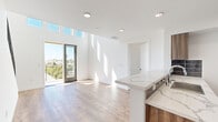 This thoughtfully designed single-floor residence showcases a clean, contemporary aesthetic highlighted by striking double-height ceilings and expansive clerestory windows in the main living area. The soaring walls are finished in crisp white, amplifying natural light that floods the space and casts dramatic patterns across the light-toned hardwood floors found throughout. A sliding glass door opens directly to a private balcony, offering elevated outdoor views of the surrounding neighborhood and treetops.

The open-concept kitchen is outfitted with warm wood-toned cabinetry, a bold dark tile backsplash, and a full suite of stainless steel appliances including a gas range, built-in microwave, and a large side-by-side refrigerator. A peninsula with a quartz-style marble countertop provides additional prep space and casual seating, seamlessly connecting the kitchen to the living area.

The bedrooms are bright and well-proportioned, each featuring hardwood flooring, white walls, and generous closet space with built-in shelving and frosted sliding doors. The bathroom is finished with large-format tile in the tub/shower surround, glass sliding shower doors, and a clean, minimalist design. Recessed lighting throughout the unit ensures consistent illumination, complementing the abundant daylight that defines this modern residence.