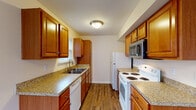 This single-story unit at 5204 B103 in Louisville, Kentucky offers a well-organized layout designed for everyday comfort. The galley-style kitchen is a functional highlight, featuring warm honey-toned cabinetry with ample upper and lower storage, granite-look countertops, and wood-look vinyl flooring. White appliances including an electric range, refrigerator, and dishwasher are complemented by a stainless steel over-the-range microwave. A window above the sink allows natural light to brighten the workspace.

The living and dining area features rich dark wood-look flooring and is filled with natural light through a large window and a sliding glass door fitted with vertical blinds, providing outdoor views and direct exterior access. The bedrooms are carpeted for comfort, with neutral warm-toned walls. One bedroom includes a spacious walk-in closet outfitted with wire shelving and hanging rods for generous storage capacity.

The bathroom is clean and efficiently designed, featuring a wood-look vinyl floor, a single-sink vanity with wood cabinetry, a mirror, and a tub-shower combination. Throughout the unit, consistent neutral tones and practical finishes create a cohesive, move-in-ready atmosphere.
