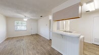 Located at 2725 SW 27th Ave in Gainesville, FL, this single-floor unit offers a practical and well-organized layout with a clean, neutral aesthetic throughout. Wood-look flooring runs continuously across the living, dining, and bedroom areas, lending a cohesive and easy-to-maintain finish to the space.

The open living area is bright and airy, featuring ceiling fans with integrated lighting and multiple windows that allow natural light to flow in. A sliding glass door provides access to the outdoors, while an additional high window adds ventilation and light without sacrificing wall space. The living area connects seamlessly to a dining space, creating a comfortable open-plan feel.

The kitchen is efficiently designed with ample white cabinetry extending to the ceiling for generous storage, white appliances including an electric range and refrigerator, and a dishwasher. A pass-through counter with an overhead shelf opens to the living and dining area, enhancing the sense of connectivity and space.

The bedroom is well-proportioned, featuring a ceiling fan, a window with outdoor views of surrounding greenery, and wood-look flooring consistent with the rest of the unit. The bathroom is cleanly appointed with a full-size tub and shower combination with white tile surround, complemented by neutral wall tones and wood-look flooring.