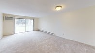 Located at 750 Farm Rd in Marlborough, MA, this single-floor residence presents a functional and straightforward layout designed for comfortable everyday living. The living area is generously proportioned, featuring neutral-toned wall-to-wall carpeting, baseboard heating, and a sliding glass door that opens to an outdoor view, allowing natural light to fill the space. The galley-style kitchen is efficiently arranged with white cabinetry accented by wood trim, white appliances including a refrigerator, electric range, and dishwasher, a stainless steel sink, and light tile flooring. Ample upper and lower cabinet storage makes the kitchen both practical and organized. The bedrooms continue the neutral carpeting found throughout, each offering closet storage—one room features mirrored sliding closet doors, while another includes a standard bifold closet. Each bedroom benefits from natural light via windows with blinds and baseboard heating. The bathroom includes a wide vanity with a single basin sink, a large mirror, and wood-trimmed cabinetry consistent with the overall design language of the unit. Throughout the space, the palette remains light and neutral, contributing to a clean, understated ambiance well-suited to a variety of furnishing styles.