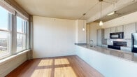 This single-floor studio unit in Memphis, TN offers an efficiently designed open-concept layout that maximizes its well-proportioned footprint. The living area features warm hardwood flooring that extends throughout the space, complemented by an abundance of natural light streaming through a bank of large double-hung windows that frame elevated views of the surrounding Memphis cityscape.

The kitchen is a functional centerpiece of the unit, featuring a peninsula with granite countertops that doubles as a breakfast bar and separates it from the living area. Gray cabinetry provides ample storage, while stainless steel appliances—including a refrigerator, range, microwave, and dishwasher—complete the well-appointed cooking space. Pendant lighting hangs above the peninsula, adding a refined touch to the area.

The exposed structural elements on the ceiling, including visible beams and piping, lend an industrial character consistent with an urban loft aesthetic. The bathroom is notably upscale, showcasing a walk-in glass shower clad in large-format, richly veined marble-look tile, adding a luxurious contrast to the unit's industrial design sensibility. Overall, the space balances contemporary finishes with urban character.