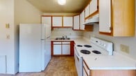 Located in Radford, Virginia, this single-floor unit offers a straightforward and functional layout across multiple rooms. The living area is generously sized, featuring soft wall-to-wall carpeting and a wide window fitted with horizontal blinds that frames a pleasant outdoor view of the surrounding greenery and street. A baseboard heating system runs along the wall, providing efficient climate control throughout the space.

The kitchen is designed for practicality, featuring white cabinetry with warm wood-toned trim, ample upper and lower cabinet storage, white appliances including a refrigerator and electric range, a double-basin sink, and durable tile flooring. An overhead range hood and a textured ceiling add to the kitchen's functional character.

Multiple carpeted rooms serve as flexible living or sleeping spaces, each benefiting from natural light through windows with views of the neighborhood's lush, tree-lined surroundings. The rooms are finished with neutral-toned walls, creating a clean and versatile backdrop.

The bathroom includes a full-size tub and shower combo with classic tile surround in soft tones, complemented by a standard toilet and textured walls. Throughout the unit, the design is clean, practical, and move-in ready, making it a solid option for comfortable everyday living in Radford, VA.
