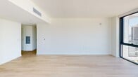 Located in the heart of downtown Miami, this modern high-rise unit offers four bedrooms and one bathroom across a thoughtfully designed single-floor layout. Light wood flooring runs throughout, complementing the clean, minimalist aesthetic defined by crisp white walls and contemporary finishes.

The open-concept living area and kitchen are anchored by expansive floor-to-ceiling windows that frame breathtaking panoramic views of the Miami skyline, with glimpses of the water beyond. A distinctive exposed concrete structural column adds an industrial design element to the living space. The kitchen is outfitted with sleek white cabinetry, stainless steel appliances including a refrigerator, range, microwave, and dishwasher, and flows seamlessly into the living area.

Each of the four bedrooms benefits from generous natural light, with several featuring their own floor-to-ceiling sliding glass doors that open to city views. The primary bedroom offers a comfortable, well-proportioned space. A central hallway lined with built-in closets connects the bedrooms efficiently. The bathroom features large-format gray tile, a glass-enclosed walk-in shower, and modern fixtures. The overall ambiance is bright, airy, and contemporary, ideal for urban living in one of Miami's most vibrant neighborhoods.