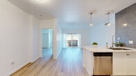 Located on Cahuenga Boulevard West in Los Angeles, this 2-bedroom, 2-bathroom residence offers a well-designed single-floor layout with a clean, modern aesthetic throughout. Light wood flooring runs continuously through the living areas and bedrooms, contributing to a bright and cohesive feel. The open kitchen is outfitted with white shaker cabinetry, light stone countertops, stainless steel appliances including a refrigerator, range, and over-the-range microwave, and a textured gray tile backsplash that adds visual contrast. The living room features sliding glass doors that open onto a private balcony overlooking lush greenery, bringing in abundant natural light and outdoor views. Both bedrooms are well-proportioned with large windows framing views of the surrounding landscape; the primary bedroom offers a comfortable, airy atmosphere, while the second bedroom includes a sliding closet for additional storage. The two bathrooms are finished with mosaic tile flooring and glass-enclosed walk-in showers with neutral ceramic tile surrounds. A hallway connects the rooms, completing the functional and efficient floor plan. The overall ambiance is clean, bright, and move-in ready, well-suited for comfortable urban living in the heart of Los Angeles.