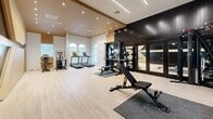 Located at 3303 Southern Oaks Blvd in Dallas, TX, this well-appointed fitness center offers a thoughtfully designed workout environment within a generously proportioned single-level space. The interior showcases a contemporary aesthetic defined by light-toned hardwood-style flooring, crisp white walls accented by warm gold tones, and a striking dark wood panel feature wall that anchors the strength training zone with bold visual contrast.

The fitness floor is equipped for a comprehensive range of workouts. A cardio section along the windowed wall houses multiple treadmills and elliptical machines, with arched windows allowing natural light to fill the space. A dedicated strength training area features a multi-functional cable and rack system, an adjustable weight bench, and a tiered dumbbell rack displayed beneath a decorative art panel. A rowing machine rounds out the cardio offerings.

Overhead, recessed can lighting and sleek linear LED fixtures provide bright, even illumination throughout. The ceiling height adds an open, airy feel to the workout environment. Full-length mirrors along the strength wall expand the perceived space and allow users to monitor their form during exercise. Dark-framed glass doors complete the polished, modern look, making this fitness center a functional and visually striking training facility.