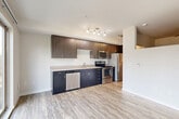 Located in Shoreline, WA, this well-designed one-bedroom, one-bathroom unit offers a thoughtful layout across a single floor. The open-concept main area seamlessly combines the living room, dining space, and kitchen, creating a bright and functional hub for daily living. The kitchen is outfitted with dark lower cabinetry, wood-toned upper cabinets, light countertops, and a full suite of stainless steel appliances including a dishwasher, range, microwave, and refrigerator. Light wood-style luxury vinyl plank flooring runs throughout the main living areas, lending a clean, contemporary aesthetic. A well-lit hallway connects the entrance to the rest of the unit, lined with sliding wood-panel doors that lead to two closets, providing ample storage. The bedroom is carpeted and features large sliding glass doors that open to a private balcony, filling the space with natural light and offering pleasant outdoor views of the surrounding neighborhood. The combined bathroom and laundry room is finished with matching light-tone flooring, a floating dark vanity with a white countertop, and a full bathtub with grab bars. The unit's modern finishes and efficient use of space make it a practical and stylish residence.