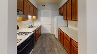 Located at 1462 E College Ave in Normal, Illinois, this single-floor unit presents a clean, functional layout well-suited for everyday living. The main living area is generously proportioned, featuring wall-to-wall carpet, neutral white walls, and dark wood baseboards that provide a subtle contrast throughout. A ceiling fan with a light fixture illuminates the space, while vertical blinds on a sliding glass door allow for natural light and outdoor access. The layout opens naturally between the living and adjoining areas, defined by a structural beam overhead that adds architectural interest.

The galley-style kitchen is efficiently designed, with warm wood cabinetry lining both sides, white countertops, and durable wood-look vinyl flooring. It is equipped with a gas range and a full-size refrigerator, along with a double-basin sink and ample cabinet storage. A louvered pantry door provides additional storage at the end of the kitchen.

The bedroom offers comfortable proportions with soft carpeting, neutral-toned walls, and a double-door closet with built-in shelving. A floor vent and easy hallway access add to the room's practicality.

The full bathroom is finished with wood-look vinyl flooring, a single-sink vanity with a mirror, and a tiled shower-tub combo equipped with grab bars for added accessibility. The space is straightforward and well-maintained throughout.