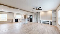 This single-story, 3-bedroom, 2-bathroom home offers a thoughtfully designed layout that balances functionality with modern farmhouse style. The open-concept kitchen and living area serves as the heart of the home, featuring light wood-look luxury vinyl flooring that flows seamlessly throughout the main living spaces. The kitchen is outfitted with crisp white cabinetry, a farmhouse-style sink, a central island with a neutral countertop, black appliances including a refrigerator, range, and dishwasher, and a charming barn-style interior door that adds a rustic touch. Recessed lighting and a decorative wood beam accent the ceiling, enhancing the warm, contemporary aesthetic. The living room is highlighted by a striking built-in shelving and entertainment unit, a ceiling fan, and large windows that invite natural light. The three bedrooms feature plush carpeting and ceiling fans, with the primary bedroom offering a generous walk-in closet equipped with wire shelving and a small window for ventilation. The two bathrooms include a tub/shower combination. A convenient built-in mudroom-style bench and shelving unit near the entry adds practical storage. The hallway connects all rooms efficiently, completing this cohesive and comfortable single-floor layout.