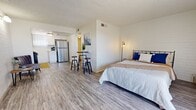 This efficiently designed studio offers a smartly organized single-floor layout that maximizes every square foot. The open-plan main area seamlessly integrates the sleeping, dining, and living zones, all unified by light gray wood-look vinyl plank flooring that runs throughout. A textured ceiling adds architectural character, while white-painted walls and a striking shiplap accent wall behind the sleeping area contribute a clean, modern aesthetic. A vertical-blind window allows natural light to filter into the main space, brightening the interior.

The kitchen is tucked into its own defined nook and is well-appointed with crisp white shaker cabinetry, white subway tile backsplash, stainless steel appliances including a full-size refrigerator and range, and ample counter space. A window above the sink brings in additional natural light, enhancing the kitchen's functional appeal.

A compact high-top table with bar stools serves as a versatile dining and work area positioned between the kitchen and sleeping zone, making efficient use of the open floor plan. The bathroom features a full tub-shower combo with white tile surround and matching flooring. A walk-in closet with built-in shelving and hanging rods provides organized storage, rounding out this thoughtfully utilized studio space.