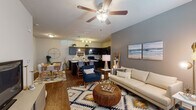 This single-floor residence offers a thoughtfully designed open-concept layout that seamlessly connects the living, dining, and kitchen areas. The living room features wood-look flooring, a ceiling fan with lighting, and large windows that invite natural light, creating a bright and welcoming atmosphere. Neutral and gray accent walls provide a modern backdrop throughout the space.

The kitchen is equipped with dark espresso cabinetry extending to the ceiling for ample storage, granite-style countertops, a kitchen island with bar seating, pendant lighting, and black appliances including a refrigerator, range, and microwave. A dedicated dining area sits adjacent, completing the open entertaining space.

The bedroom is carpeted and comfortably sized, featuring a ceiling fan, a large window with outdoor views, and a gray accent wall. Two full bathrooms are present in the unit, each featuring dark vanity cabinetry with granite-style countertops, a tub-shower combination, wood-look flooring, and a large mirror.

A dedicated laundry area houses a full-sized top-loading washer and dryer with overhead shelving, adding everyday convenience to the unit's practical layout.