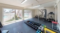 This single-level fitness center is a comprehensively outfitted exercise space designed to support a wide range of workout routines. The room features durable rubber flooring throughout, providing a safe and functional surface for both weightlifting and cardio activities. Large floor-to-ceiling mirrors line one wall, enhancing the sense of space and allowing users to monitor their form during exercise.

Natural light fills the room through sliding glass doors that open directly to an outdoor pool area, offering views of lush greenery, a swimming pool, and surrounding landscaping. Fluorescent overhead lighting supplements the natural light, ensuring the space is well-lit at all times.

The fitness center is equipped with a multi-station cable machine, a flat weight bench, a treadmill, an elliptical trainer, and a stair-climber-style cardio unit. A full rack of dumbbells in varying weights is neatly arranged on the floor, alongside exercise mats, resistance equipment, and a stability ball. A dedicated stretching and functional training zone provides additional versatility. The overall ambiance is practical and energetic, making it a functional facility for residents seeking convenient on-site fitness amenities.