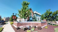 Georgetown Square presents a striking architectural presence defined by its warm red brick exterior, accented by light-colored siding and a series of large, multi-pane windows that allow generous natural light throughout the building. The structure rises multiple stories, featuring dormered rooflines that add a classic, residential character to the overall design. The facade combines traditional and contemporary elements, with arched window detailing and clean geometric lines that give the building a refined, timeless appearance.

The community's exterior is thoughtfully landscaped, with mature trees providing natural shade and seasonal color, complemented by well-maintained mulched garden beds filled with flowering plants and decorative shrubs. A prominent brick monument sign at the entrance boldly identifies the development as Georgetown Square, serving as a welcoming landmark for residents and visitors alike. Classic black lamppost streetlights line the walkways, reinforcing the neighborhood's traditional aesthetic. Banners mounted along the street add a sense of community identity and vibrancy. The overall ambiance is one of an established, carefully curated community that balances architectural elegance with approachable, neighborhood-oriented charm.