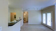 This single-story space in Duncanville, Texas offers a cohesive open layout that connects the kitchen and living areas seamlessly. A peninsula-style breakfast bar with a dark granite countertop serves as a natural divider between the kitchen and the main living space, providing both functionality and definition. The kitchen area is visible through a pass-through opening, adding to the open, connected feel of the interior.

The living area is finished with neutral-toned carpet flooring and crisp white walls, creating a clean and versatile backdrop. Crown molding runs along the upper perimeter of the room, adding a subtle architectural detail. Track lighting with adjustable fixtures is mounted on the ceiling, offering flexible, directed illumination throughout the space.

A graceful arched doorway leads to a hallway beyond, where warm wood-toned cabinetry is visible, suggesting access to additional rooms. Natural light filters in through a window with horizontal blinds on the right side of the living area. The overall ambiance is bright, neutral, and well-maintained, offering a practical and welcoming single-level layout.
