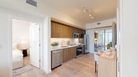 Located at 225 SW Tenth Street in Miami's vibrant Brickell neighborhood, this modern 2-bedroom, 3-bathroom residence offers a well-designed single-floor layout with clean lines and contemporary finishes throughout. The open-concept kitchen is a standout feature, showcasing rich wood-grain cabinetry extending to the ceiling, a white quartz countertop with subway tile backsplash, and a full suite of stainless steel appliances including a side-by-side refrigerator with ice maker, range, microwave, and dishwasher. Light hardwood flooring flows seamlessly from the kitchen into the dining and living areas, complemented by track lighting overhead. A compact dining nook adjacent to the kitchen features a built-in table with upholstered chairs, making efficient use of space. Each bedroom is finished in a neutral palette with light wood floors and direct access to a bathroom. The primary bedroom connects to an en-suite bath. All three bathrooms maintain a consistent modern aesthetic, featuring wood-finish vanities, white quartz countertops, large mirrors, and light tile flooring. Two dedicated closets provide organized storage with built-in shelving and hanging rods. The overall ambiance is bright, clean, and contemporary, reflecting Miami's modern urban residential design.