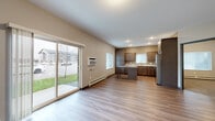 Located at 2407 CR-74 in Saint Cloud, Minnesota, this well-appointed one-bedroom, one-bathroom unit offers a practical and modern single-floor layout. The open-concept living and kitchen area is bright and inviting, anchored by durable wood-style plank flooring throughout. A large sliding glass door floods the living room with natural light and provides direct access to a ground-level patio with outdoor views of the surrounding green space.

The kitchen is thoughtfully designed with rich dark wood cabinetry, granite-style countertops, stainless steel appliances including a refrigerator and dishwasher, and a central island that doubles as a dining or prep space. A hallway with a stylish barn-style door leads to the private areas of the unit, including a dedicated laundry closet equipped with a stacked full-size washer and dryer.

The bedroom features soft wall-to-wall carpeting, a bright window with blinds, and baseboard heating for year-round comfort. The bathroom offers a clean, contemporary feel with dark wood vanity cabinetry, white countertops, and wood-style flooring. A dedicated closet provides additional storage. Neutral wall tones and consistent finishes throughout give the space a cohesive, move-in-ready appeal.