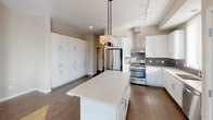 Located at 116 E Hennepin Ave in Minneapolis, this single-floor residence offers a thoughtfully designed layout with contemporary finishes throughout. The kitchen serves as a central highlight, featuring white shaker cabinetry, a large marble-topped island, stainless steel appliances including a gas range and built-in refrigerator, a sleek wall-mounted range hood, dark tile backsplash, and a pendant light fixture overhead. Extensive floor-to-ceiling pantry cabinetry provides generous storage. Rich hardwood flooring extends through the main living areas, leading to a spacious living room filled with natural light from oversized windows. A modern fireplace anchors the living space, adding warmth and visual interest. Bedrooms feature plush carpeting, ceiling fans, and large windows that invite abundant natural light. The primary bathroom is well-appointed with dual vanity sinks, backlit mirrors, marble-look countertops, a walk-in shower, soaking tub, and neutral tile flooring. A secondary bathroom mirrors the refined aesthetic with its own backlit mirror and marble-look vanity. A walk-in closet with built-in shelving and hanging rods offers substantial storage capacity. A dedicated laundry room with full-size washer and dryer completes this well-appointed residence.