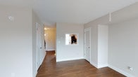 Located in Charlestown, this two-floor space offers a clean, modern aesthetic defined by neutral tones and practical design choices throughout. The interior is finished with rich, dark hardwood flooring that runs continuously through the main living areas, providing warmth and contrast against the crisp white trim and light grey walls.

A notable architectural detail is the interior pass-through window, which connects the main living area to the kitchen, promoting an open sightline while maintaining defined zones. This feature enhances the sense of connectivity between spaces without fully opening the floor plan. The kitchen, visible through the pass-through, includes cabinetry and appliances that complement the overall design.

White panel doors with consistent hardware provide access to closets and adjoining rooms, including a louvered-door closet that adds functional storage. The hallway extends toward additional rooms, suggesting a well-distributed layout across the floor. Ceiling-mounted lighting provides ambient illumination throughout. White baseboards frame each room cleanly, reinforcing the cohesive, well-maintained finish of the space. Spread across two floors, the home offers ample room for varied living arrangements.