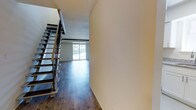 This two-story townhouse offers a practical and well-appointed layout across two floors, featuring 2 bedrooms and 2.5 bathrooms. The main level is characterized by rich, dark hardwood flooring that extends throughout the open living area, creating a warm and inviting atmosphere. A striking staircase with a sleek metal railing and wooden accents serves as a functional architectural focal point, connecting the two floors with style. Large sliding glass doors at the rear of the main living area flood the space with natural light and provide views of the outdoors, enhancing the sense of openness. The neutral, warm-toned walls complement the flooring and contribute to a clean, versatile aesthetic throughout. The two-floor configuration provides a natural separation between the living and sleeping areas, offering added privacy and functionality. With 2.5 bathrooms, the layout conveniently accommodates both residents and guests. The overall design balances contemporary finishes with a comfortable, livable feel, making this townhouse a well-rounded space suited for a variety of lifestyles.