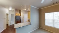 This single-floor residence offers a thoughtfully designed layout with a seamless flow between its main living areas. The kitchen is a functional highlight, featuring warm honey-toned cabinetry, granite countertops, stainless steel appliances including a refrigerator, electric range, and built-in microwave, as well as rich hardwood-style flooring. A granite-topped breakfast bar connects the kitchen to the adjacent living and dining areas, making it ideal for both everyday meals and casual entertaining. The living and dining spaces are finished with the same hardwood-style flooring, crown molding, a ceiling fan, and a pendant light, creating a cohesive and welcoming atmosphere. Natural light filters in through windows fitted with blinds throughout the unit. The bedroom areas are carpeted for comfort, each with standard lighting and windows that allow for ample daylight. The bathroom is clean and practical, featuring a full tiled tub-and-shower combination with brushed nickel fixtures. A dedicated in-unit laundry room provides added convenience, housing a full-size side-by-side washer and dryer set along with a wall-mounted storage shelf. Overall, the space presents a functional and comfortable living environment with consistent finishes throughout.