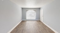 Located at 3201 E Park Row Dr in Arlington, TX, this single-floor residence offers a clean, modern aesthetic throughout. The interior is painted in a soft gray-blue palette that lends a calm, cohesive feel to each room. Wood-look plank flooring runs through the main living areas and kitchen, providing a durable and attractive finish, while plush carpet adds warmth to the bedrooms.

The living area is bright and open, featuring a charming arched window that invites natural light and a textured ceiling that adds subtle architectural character. The kitchen is efficiently laid out and equipped with black appliances — including a refrigerator, range, and over-the-range microwave — complemented by white cabinetry and a light countertop.

The bedrooms are generously sized, each featuring ceiling fans with light fixtures and arched windows that frame outdoor views. The primary bedroom includes a walk-in closet with dual shelving systems and direct access to a private bathroom. An additional full bathroom serves the rest of the unit, both finished with white tiled tub-shower combinations, wood-look flooring, and clean white vanities. The layout as a whole is functional and well-organized, making efficient use of the available space.