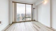 Located on Wilshire Boulevard in the heart of Los Angeles, this modern single-floor unit offers a well-designed open layout that maximizes its compact footprint. Light wood-tone flooring runs throughout, complementing the clean white walls and creating a bright, cohesive aesthetic.

The open-concept kitchen and living area serves as the centerpiece of the space. The kitchen is outfitted with stainless steel appliances — including a French door refrigerator, gas range, microwave, and dishwasher — paired with two-toned cabinetry featuring dark wood lower cabinets and light upper cabinets. A gray mosaic tile backsplash adds texture, while a central island with a white countertop provides additional workspace and storage.

Floor-to-ceiling windows in the living area flood the space with natural light and frame impressive panoramic views of the Los Angeles skyline, offering a striking urban backdrop. The living room is open and airy, offering ample flexibility for furnishing arrangements.

The bathroom is well-appointed with a wide dark wood vanity, white countertop, a large mirror, and a combination tub and shower enclosed with glass doors. A window in the bathroom also captures city views. Two dedicated closet spaces provide practical storage throughout the unit.