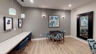 Located at 5100 Quail Run Rd in Riverside, California, this single-floor amenity space offers a well-appointed collection of functional areas designed to support the needs of its residents. Light wood-look flooring flows throughout, creating a cohesive and welcoming atmosphere across each zone.

The mail and package room is easily accessible and equipped with an array of parcel lockers and mailboxes, accented by a teal feature wall and a decorative potted plant that adds a touch of greenery. A glass-paneled entrance provides a seamless transition into this practical space.

The co-working lounge is thoughtfully designed with a long, marble-top counter workspace running along one wall, outfitted with power outlets for convenience. A series of striking framed silhouette artworks hang above the counter, illuminated by a row of elegant teal pendant lights. Teal accent chairs complete the stylish yet productive setting.

Adjacent to the lounge is a private meeting or study room featuring a dark rectangular table surrounded by patterned blue-and-white chairs. Wall sconces and recessed lighting provide warm, focused illumination, while a framed abstract artwork adds a decorative touch. Large floor mirrors visually expand the space and reflect the lounge beyond. A window connects the room to neighboring areas, enhancing the open, collaborative feel of the overall layout.