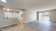 This single-floor residence offers a thoughtfully designed open-concept layout that connects the living, dining, and kitchen areas into one cohesive space. Light wood-look flooring runs throughout the main living areas, complemented by neutral warm-gray walls and a textured ceiling that adds subtle visual interest. A sliding glass door in the living area floods the space with natural light and provides access to an outdoor balcony.

The kitchen is well-equipped with white shaker-style cabinetry, granite countertops, a tiled subway backsplash, stainless steel appliances including a range, over-the-range microwave, and refrigerator, and a raised peninsula with a gold-tone faucet that doubles as a casual dining or prep area.

The bedroom is generously sized, featuring plush neutral carpet, a ceiling fan with light fixture, and two windows that bring in ample natural light. A panel door leads from the bedroom into the hallway connecting to the rest of the unit.

Two bathrooms complete the layout. One bathroom includes a granite-topped vanity, wood-look flooring, and a toilet with grab bar support. The second bathroom features a granite vanity, tiled tub-shower combination, and matching hardware. The entry foyer is open and welcoming with clean finishes and an intercom panel near the front door.