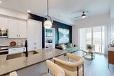Located at 1901 Presidential Way in West Palm Beach, this thoughtfully designed two-bedroom, three-bathroom residence offers a refined modern aesthetic across a well-proportioned single-floor layout. The open-concept kitchen and living area serves as the heart of the home, anchored by a striking navy accent wall that adds bold contrast to the otherwise bright, white interior. The kitchen features white shaker cabinetry, a marble-style tile backsplash, stainless steel appliances, and a generous quartz-topped island with seating for multiple bar stools, illuminated by contemporary globe pendant lights. Light wood-look flooring flows throughout, complementing the clean lines and neutral palette. The living area benefits from large sliding glass doors that invite natural light and provide outdoor views of the West Palm Beach skyline. The spacious primary bedroom includes floor-to-ceiling windows with outdoor views, a deep green accent wall, an en-suite bathroom with a dual-sink white vanity, matte black fixtures, a large framed mirror, and a walk-in closet with built-in shelving. The second bedroom is equally well-appointed. Three full bathrooms, two dedicated closets, and a ceiling fan in the living area round out the practical features of this polished residence.
