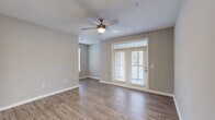 Located at 80 Oak Ave in Mount Pleasant, SC, this well-appointed two-bedroom, two-bathroom residence offers a thoughtfully designed single-floor layout. The open-concept kitchen and living area serves as the heart of the home, featuring wood-look luxury vinyl plank flooring throughout the main areas. The kitchen is equipped with white shaker-style cabinetry, stainless steel appliances including a refrigerator, range, and microwave, and a peninsula with a white countertop and undermount sink — ideal for casual dining or meal prep. The living room is bright and airy, highlighted by a ceiling fan, neutral gray walls, and French doors that provide outdoor access and an abundance of natural light. A connecting hallway with additional storage access links the main living areas to the private quarters. Both bedrooms are carpeted and finished in soft neutral tones; the primary bedroom includes an en-suite bathroom and direct access to a spacious walk-in closet with wire shelving on multiple levels. The bathrooms feature white vanities, light countertops, and tub-shower combinations with tile surrounds. Wood-look flooring continues through the hallways, tying the overall aesthetic together for a clean, cohesive look throughout.