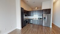 Located at 5402 Middle Fiskville Rd in Austin, Texas, this single-floor unit offers a thoughtfully designed layout with modern finishes throughout. The kitchen is a standout feature, equipped with stainless steel appliances including a range, dishwasher, side-by-side refrigerator with ice and water dispenser, and microwave. Gray shaker-style cabinetry with dark upper accent cabinets provides ample storage, complemented by granite-look countertops and a white subway tile backsplash. Wood-style flooring runs throughout the main living areas, adding warmth and continuity to the space.

The living area is generously proportioned, featuring neutral walls, a ceiling fan, and a glass sliding door alongside stacked square windows that invite natural light. The open floor plan connects the kitchen and living spaces seamlessly. The bedroom is carpeted for comfort and connects to a well-appointed bathroom featuring dark wood cabinetry, granite-look countertops, and continued wood-style flooring. A closet and additional storage areas are accessible from the bedroom corridor, enhancing the unit's functionality. The overall aesthetic is clean, contemporary, and move-in ready.