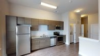 Located at 131 E Davie St in the heart of downtown Raleigh, North Carolina, this modern single-floor space offers a clean, contemporary design with thoughtful finishes throughout. The kitchen serves as a standout feature, equipped with a full suite of stainless steel appliances including a refrigerator, electric range, built-in microwave, and dishwasher. Sleek wood-tone cabinetry lines the walls both above and below the countertops, which feature a light granite-style surface that adds a refined touch. A double-basin sink is centrally positioned along the cabinetry wall, complementing the efficient and functional layout. The flooring throughout is a warm hardwood-style material that adds continuity and a modern aesthetic to the space. Bright overhead lighting ensures the kitchen and surrounding areas are well-illuminated. White walls provide a crisp, neutral backdrop that enhances the open feel of the interior. A doorway visible from the kitchen hints at additional rooms beyond, suggesting a practical and well-organized floor plan. The overall ambiance is modern, clean, and move-in ready, making it well-suited for those seeking a functional and stylish space in a prime urban Raleigh location.