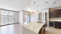 Located at 302 Axis Dr in Louisville, Kentucky, this single-floor unit presents a clean, contemporary design defined by a neutral palette and thoughtful finishes throughout. The open-concept kitchen and living area serves as the heart of the space, anchored by a generously sized island topped with quartz countertops and an undermount sink. Three elongated pendant lights hang above the island, complementing the stainless steel appliances, including a refrigerator, range, and microwave. Rich dark-espresso cabinetry lines the kitchen walls, accented by a tile backsplash and a decorative wine rack, providing striking contrast against the light countertops and pale hardwood-style flooring that flows seamlessly through the main living areas.

The living area benefits from large windows fitted with blinds, allowing abundant natural light and views of the surrounding brick exterior streetscape. Sliding glass doors open to an outdoor balcony, further enhancing the connection to the exterior.

Carpeted bedroom spaces offer a softer feel, each with bright white walls and windows that invite natural light. A spacious walk-in closet features wire shelving and carpet flooring for practical storage. The bathroom is well-appointed with a dark-cabinetry vanity, white quartz countertop, undermount sink, and a well-lit mirror framed by modern vanity lighting.