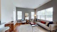 This single-floor residence offers a thoughtfully designed interior with a contemporary aesthetic. The living room serves as the central gathering space, featuring warm hardwood flooring, neutral gray accent walls, and multiple double-hung windows that allow abundant natural light and outdoor views. A large floor-length mirror enhances the sense of openness, while the layout accommodates both seating and lounge areas comfortably.

Adjacent to the living space, a cozy dining nook features hardwood flooring, a pendant chandelier, and a window overlooking the surrounding neighborhood. The kitchen is outfitted with rich cherry wood cabinetry, granite countertops, stainless steel appliances including a refrigerator, range, and microwave, and hardwood flooring that ties the space together functionally.

The primary bedroom offers plush carpeting, a bold teal accent wall, and direct access to an en-suite bathroom and additional closet space. A second bedroom mirrors this design approach with its own accent wall and ample natural light. Two bathrooms serve the residence — one full bath with a dark wood vanity and tile flooring, and a second, more compact bathroom with clean, minimal finishes throughout.