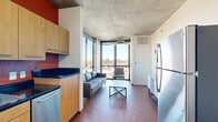 This 5-bedroom, 4-bathroom unit in Denver, CO offers a well-designed layout across a single floor. The living area makes a bold architectural statement with exposed concrete ceilings and floor-to-ceiling windows that flood the space with natural light and frame sweeping views of the Denver skyline and surrounding cityscape. The kitchen is fully equipped with stainless steel appliances — including a range, microwave, and dishwasher — complemented by warm wood cabinetry, dark granite countertops, and a rich red tile backsplash that adds a vibrant pop of color. Hardwood-style flooring runs throughout the main living and kitchen areas, adding warmth and continuity to the space. Each of the five bedrooms is carpeted and features its own private entrance via well-organized hallways. Select bedrooms enjoy direct window access with city and treetop views. The four bathrooms are consistently appointed with wood-framed vanities, white tile walk-in showers, and hardwood-style flooring, offering a clean and functional aesthetic. The unit's layout is practical and efficient, with multiple hallways ensuring clear separation between shared and private areas — making it well-suited for multi-resident living in the heart of Denver.