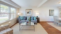 This two-story, 2-bedroom, 1-bathroom home offers a thoughtfully arranged layout that balances functionality with a warm, inviting aesthetic. The main level features rich hardwood flooring throughout the living, dining, and kitchen areas. The living room is bright and airy, with windows that bring in natural light and provide views of the surrounding greenery, complemented by clean white walls and crown molding details. Adjacent to the living space, the dining area accommodates a round dining table and is framed by additional windows, enhancing the open feel of the floor. The kitchen is well-equipped with granite countertops, warm wood cabinetry, stainless steel appliances including a gas range and dishwasher, and additional pantry storage. Upstairs, the two bedrooms are carpeted and generously proportioned. The primary bedroom features a bank of windows that flood the room with natural light and offer pleasant outdoor views, creating a serene retreat. The full bathroom is finished with tile flooring, a granite-topped vanity with dark wood cabinetry, and a shower/tub combination, accented by a natural light source from a window. A staircase with a classic wood railing connects the two levels, completing this comfortable and practical home.