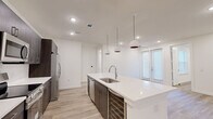 This well-appointed 2-bedroom, 2-bathroom residence offers a thoughtfully designed open-concept layout with light wood-look flooring throughout. The combined kitchen and living area serves as the heart of the home, centered around a large quartz waterfall island with an undermount sink and stylish globe pendant lighting. The kitchen is equipped with stainless steel appliances — including a French door refrigerator with ice maker, a range, and an over-the-range microwave — complemented by rich dark cabinetry that provides ample storage. The living area receives natural light through sliding glass doors that open directly onto a private patio. Both bedrooms are comfortably sized, featuring ceiling fans and recessed lighting, with the primary bedroom offering generous closet space. The two bathrooms are finished with striking marble-look wall surrounds; the primary bath includes a frameless glass walk-in shower with dark vanity cabinetry and white quartz countertop, while the secondary bath features a full tub-shower combination. Additional conveniences include in-unit laundry, four closets for abundant storage, and a clean, modern aesthetic throughout with crisp white walls and recessed lighting.