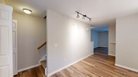 This multi-story residence spans three floors connected by carpeted staircases with warm wood handrails, offering a functional and comfortable layout throughout. The main living areas feature durable hardwood-style flooring in rich tones, complemented by neutral-toned walls that create a bright and welcoming atmosphere. Track lighting is installed in key areas, providing versatile and modern illumination.

The kitchen is well-equipped with crisp white cabinetry, dark countertops, and a full suite of white appliances including a refrigerator, range, and dishwasher. A window above the sink allows natural light to filter in, while an adjacent walk-in closet or pantry area adds convenient storage. Track lighting overhead enhances the functional workspace.

The living area is generously sized with hardwood-style flooring and a sliding glass door fitted with vertical blinds, opening to an outdoor balcony with views of surrounding greenery — a standout feature that brings natural light deep into the space.

The bedrooms are finished with plush carpeting and ceiling fans, offering comfort and airflow. Each room includes closet storage, with at least one bedroom featuring a bifold closet door. The overall design is clean and neutral, providing a move-in-ready environment with practical finishes throughout all three levels.