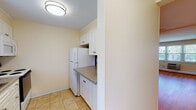 Located at 597 Millville Ave in Naugatuck, Connecticut, this multi-floor property spans three levels and offers a practical, well-organized layout throughout. The main living area features warm hardwood flooring and an open feel, with a ceiling fan overhead and a staircase connecting the levels. A pass-through opening provides a connection between the living space and the kitchen area.

The galley-style kitchen is equipped with white cabinetry, granite-look countertops, a stainless steel sink, an electric range with overhead microwave, and a full-size refrigerator. Light tile flooring runs throughout the kitchen, which also provides convenient access to an adjacent bathroom.

The bedrooms are carpeted and finished in soft neutral tones, with multiple windows fitted with blinds that allow natural light to filter in. Baseboard heating is present throughout, and at least one bedroom includes a wall-mounted air conditioning unit and a closet. The bathrooms feature tile flooring, a tub-shower combination with white tile surround, and warm wood vanity cabinetry.

The lower level consists of an unfinished basement with concrete block walls, exposed utilities, and open floor space, offering significant potential for storage or future development. Overall, the property presents a clean, functional living environment across all three floors.