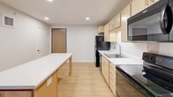 Located at 2800 N Wayzata Blvd in Minneapolis, Minnesota, this single-floor unit offers a clean, modern design with light wood flooring flowing consistently throughout every room, creating a warm and cohesive aesthetic.

The kitchen serves as a functional centerpiece, featuring light maple cabinetry, white quartz countertops, and a full suite of black appliances including a refrigerator, electric range, microwave, and dishwasher. A central island with a white countertop provides additional prep and dining space, while recessed lighting keeps the area bright and inviting.

The unit includes multiple bedrooms, each finished with the same light wood flooring and neutral gray-white walls. Several bedrooms benefit from windows overlooking the surrounding urban environment, allowing natural light to fill the space. Each room offers a clean, versatile layout suitable for a variety of furnishing arrangements, and closet access is available in select rooms.

The bathroom is thoughtfully designed with accessibility in mind, featuring multiple grab bars, a light maple vanity with a white countertop, a wall-mounted mirror, and light wood flooring that maintains continuity with the rest of the unit. The clean white walls and minimalist fixtures give the bathroom a fresh, functional feel.

Overall, the unit presents a modern, neutral palette with practical finishes throughout, well-suited for comfortable everyday living.