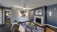 Located at 100 Heritage Point Rd. in Charlotte, NC, this single-floor residence showcases a cohesive contemporary design with warm neutral tones, dark hardwood-style flooring, and thoughtfully curated interiors throughout. The living room serves as the heart of the home, centered around a fireplace with a tile surround, ceiling fan, and an accent wall in deep navy blue that adds depth and character. Large windows invite natural light, with views of lush greenery just beyond. Adjacent to the living area, the dining space features a round glass table beneath a pendant light, framed by multiple windows dressed in layered curtains and wood blinds. The kitchen is well-appointed with white cabinetry, dark granite countertops, a mosaic tile backsplash, black appliances, and track lighting. A versatile nook off the kitchen provides a functional workspace. The bedrooms offer a calm retreat, with plush carpeting, ceiling fans, and tasteful accent walls. One bedroom includes a connected en-suite bathroom. Both bathrooms are finished with granite-topped white vanities, large mirrors with lighted fixtures, and tub-shower combinations with tile surrounds. The overall ambiance is modern, cohesive, and comfortable.
